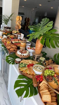 an assortment of food is displayed on a buffet table with palm leaves and potted plants