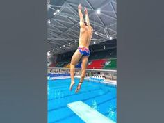 a man jumping into the water from a diving platform in an indoor swimming pool,