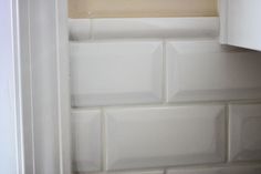 the corner of a kitchen with white tile on the wall and cupboards behind it