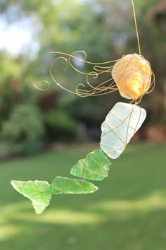 a wind chime hanging from a tree in the grass with leaves attached to it