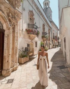 a woman is walking down the street in an old european town, wearing a white dress