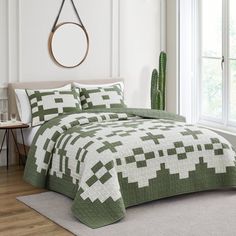 a green and white quilted bed in a bedroom next to a window with potted cacti