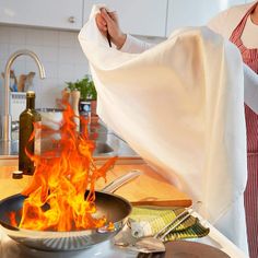 a woman in an apron holding a towel over a pan on top of a stove