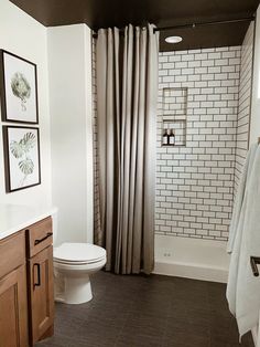 a white toilet sitting in a bathroom next to a sink and shower stall with two framed pictures on the wall