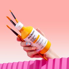 a hand holding an orange and yellow bottle with paintbrushes sticking out of it