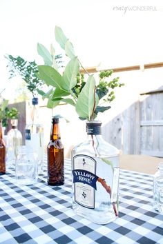 there are bottles and glasses on the table with some plants in them, one is empty