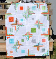 a young boy sitting on a bench holding up a large quilt made with squares and crosses