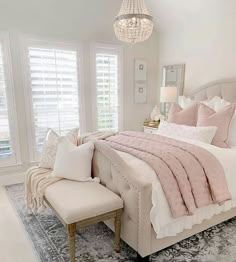 a bedroom with a large bed, chandelier and two windows that have white shutters