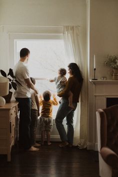 a group of people standing in front of a window next to a baby and toddler