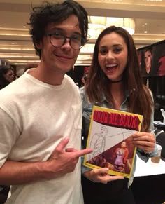 a man and woman standing next to each other in front of a table with comic books on it