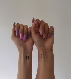 two hands with pink and purple nail polishes on their fingers, one holding up the other