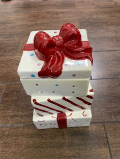 a white gift box with a red bow on it sitting on the floor next to a brown tile floor