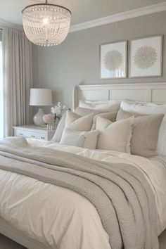 a white bed sitting in a bedroom under a chandelier next to a window