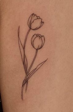 a small flower tattoo on the back of a woman's left thigh, with two tulips growing out of it