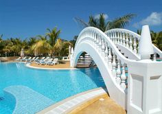 an outdoor swimming pool with white railings and chairs around the edge, surrounded by palm trees