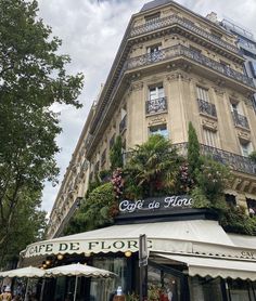 an outdoor cafe with flowers and plants on the side of it in front of a tall building