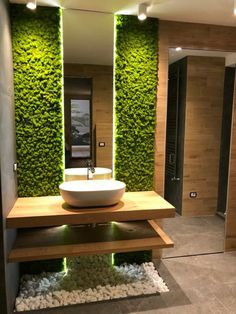 a modern bathroom with moss growing on the wall and sink in the center, surrounded by white pebbles