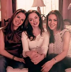 three women sitting on a couch smiling for the camera