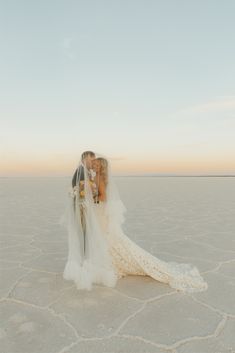 a bride and groom kissing in the middle of an empty salt flat field at sunset