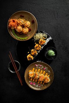 two plates filled with food next to chopsticks on a black tablecloth covered surface