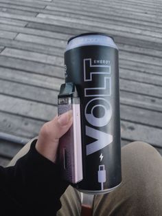 a person holding up a can of energy drink with an electronic device attached to it