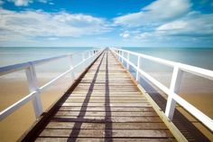 a long pier stretching out into the ocean under a blue sky with wispy clouds