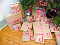 wrapped presents under a christmas tree with the word happy holidays spelled out on them in pink