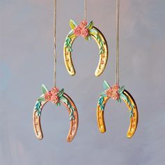 three wooden horseshoes hanging from strings with flowers and leaves painted on the sides,