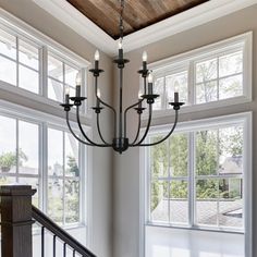 a chandelier hanging from the ceiling in a room with large windows and wooden beams