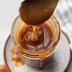 someone pouring caramel sauce into a glass jar on top of a plate with other items