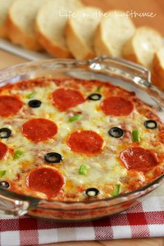 a pepperoni and olive pizza in a glass dish with slices of bread on the side