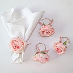 pink flowers are sitting on napkins next to white cloth and silver ring holders with bows