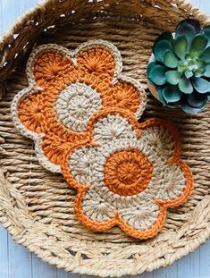 an orange and white crocheted flower on a basket next to a succulent plant