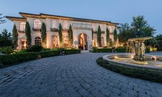 a large house with a fountain in front of it at night time, surrounded by greenery