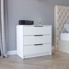 a white nightstand with two drawers and a clock on top of it next to a bed