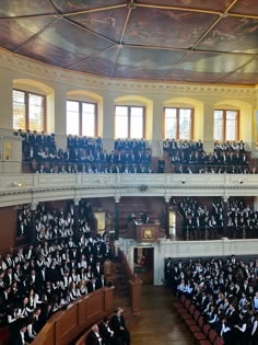 an auditorium full of people in black and white robes, with one person standing at the front of the room