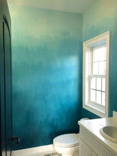 a white toilet sitting in a bathroom next to a sink under a window with blue paint on the walls