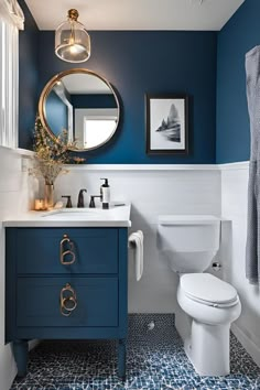 a white toilet sitting next to a blue sink in a bathroom under a round mirror