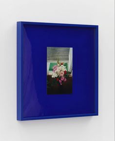 a blue frame with flowers in it hanging on the wall next to a white wall