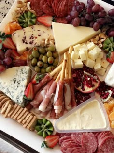 an assortment of cheeses, meats and fruit on a platter with crackers