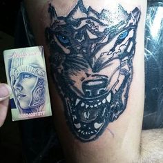 a man with a wolf head tattoo on his arm next to a playing card that is in front of him