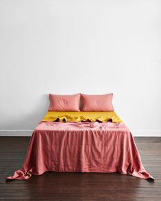 a bed with pink and yellow sheets in a white room next to a wooden floor