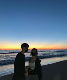 a man and woman walking on the beach at sunset