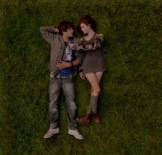 two people laying in the grass with their arms around each other and one person holding his head