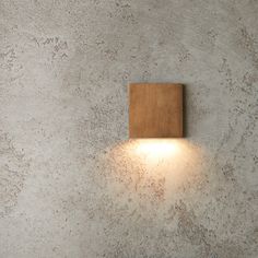 a wall light mounted on the side of a cement wall with a wooden block attached to it