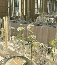 the table is set with clear vases, plates and silverware as well as flowers