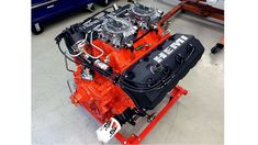 an orange engine sits in the middle of a room with other cars and trucks behind it