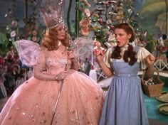 two women dressed in dresses and tiaras standing next to each other, one holding an umbrella