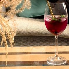 a glass filled with liquid sitting on top of a wooden table next to a plant