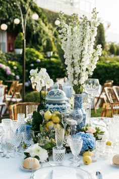 a table topped with lots of blue and white vases filled with flowers next to glasses